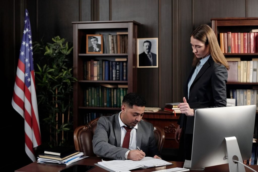 Business professionals discussing documents at a desk in an office with an American flag in the background.